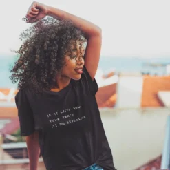 The Cost Of Peace Tee -Aurora Style Shop mockup of a curly haired woman wearing an oversized t shirt on a balcony 34951 r el2