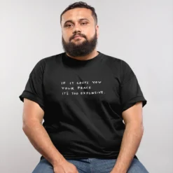 The Cost Of Peace Tee -Aurora Style Shop plus size t shirt mockup featuring a man with a beard sitting on a stool 20795